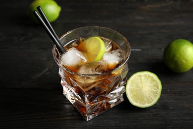 Glass of cocktail with cola, ice and cut lime on wooden background