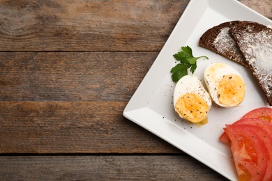 Plate with boiled egg, toasts and tomatoes on wooden background, top view. Space for text