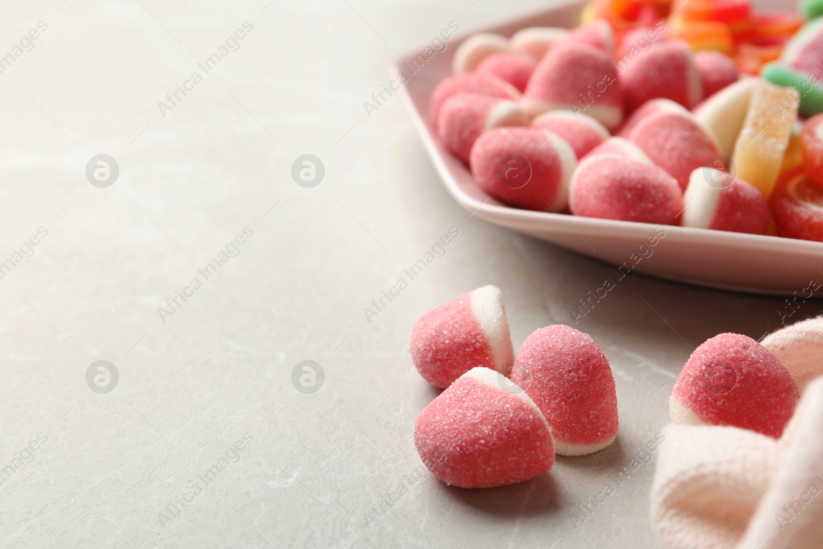 Photo of Plate of different jelly candies on light marble background. Space for text