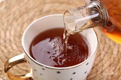 Photo of Pouring aromatic tea into cup at table, closeup