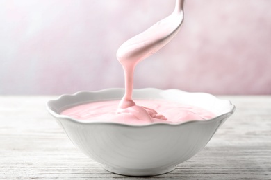 Photo of Bowl and spoon with tasty yogurt on wooden table