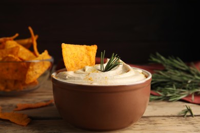 Photo of Delicious hummus with nachos and rosemary on wooden table, closeup