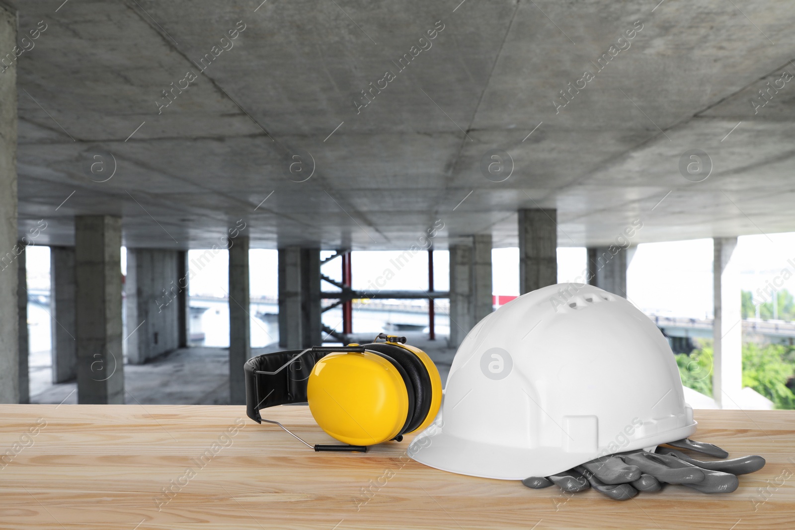 Image of Safety equipment. Hard hat, gloves and protective headphones on wooden surface inside of unfinished building, space for text