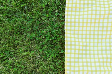 Photo of Checkered picnic tablecloth on fresh green grass, top view. Space for text