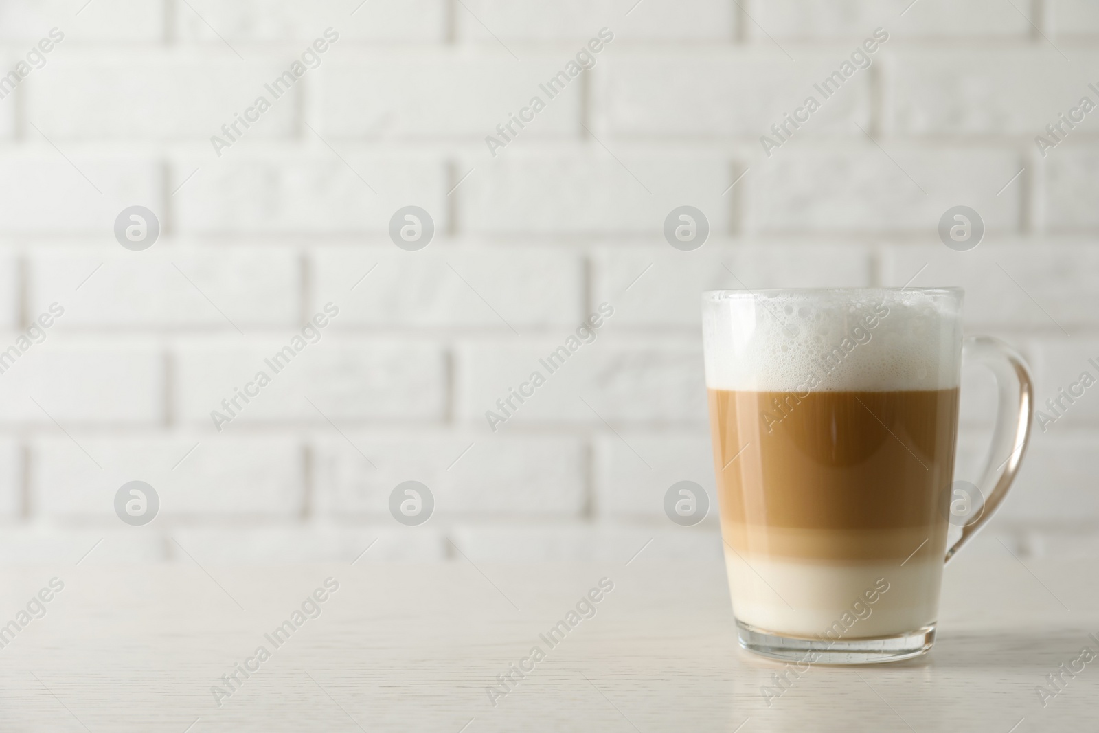 Photo of Hot coffee with milk in glass cup on white wooden table. Space for text