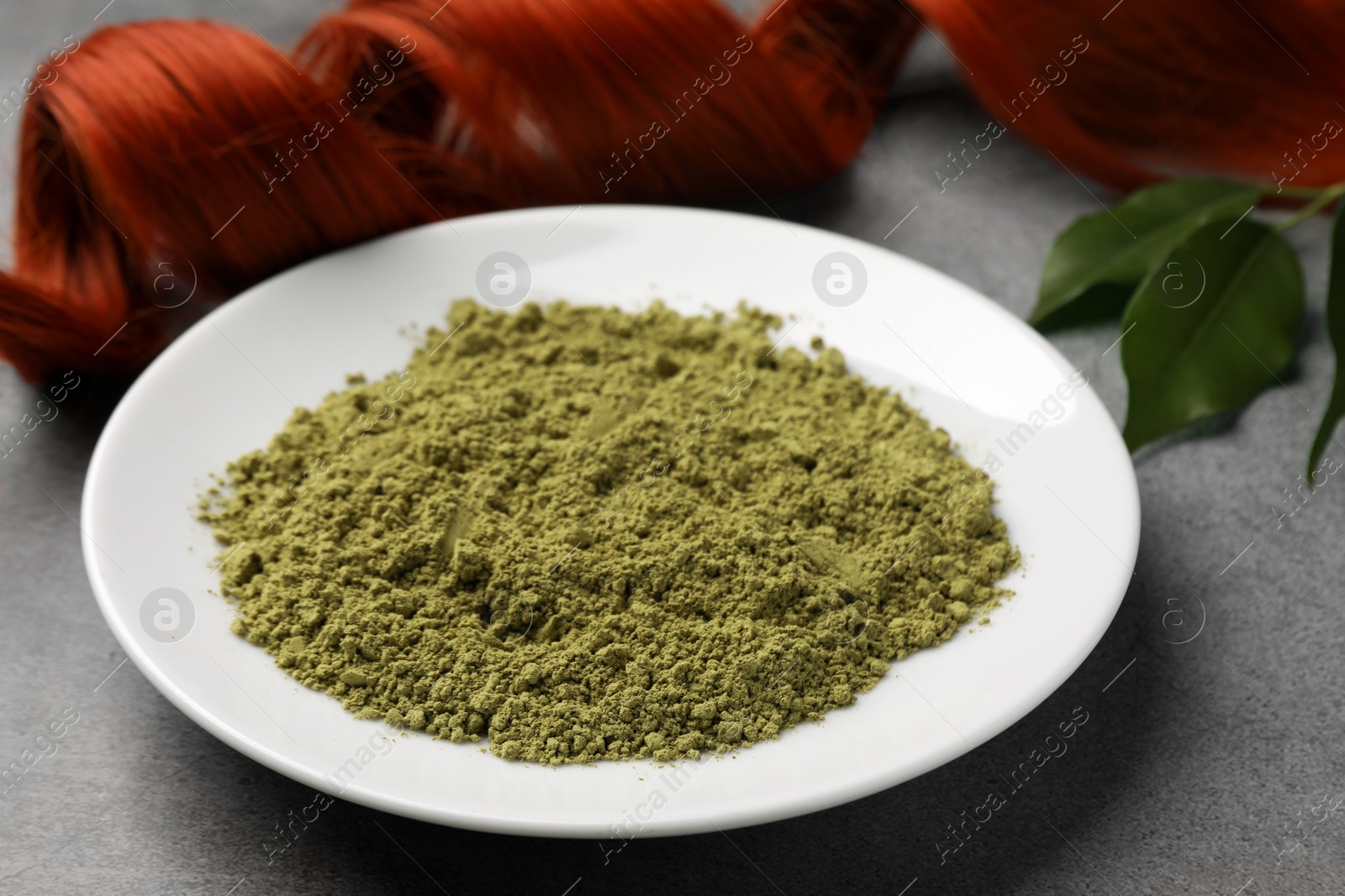 Photo of Henna powder and red strand on grey table, closeup. Natural hair coloring