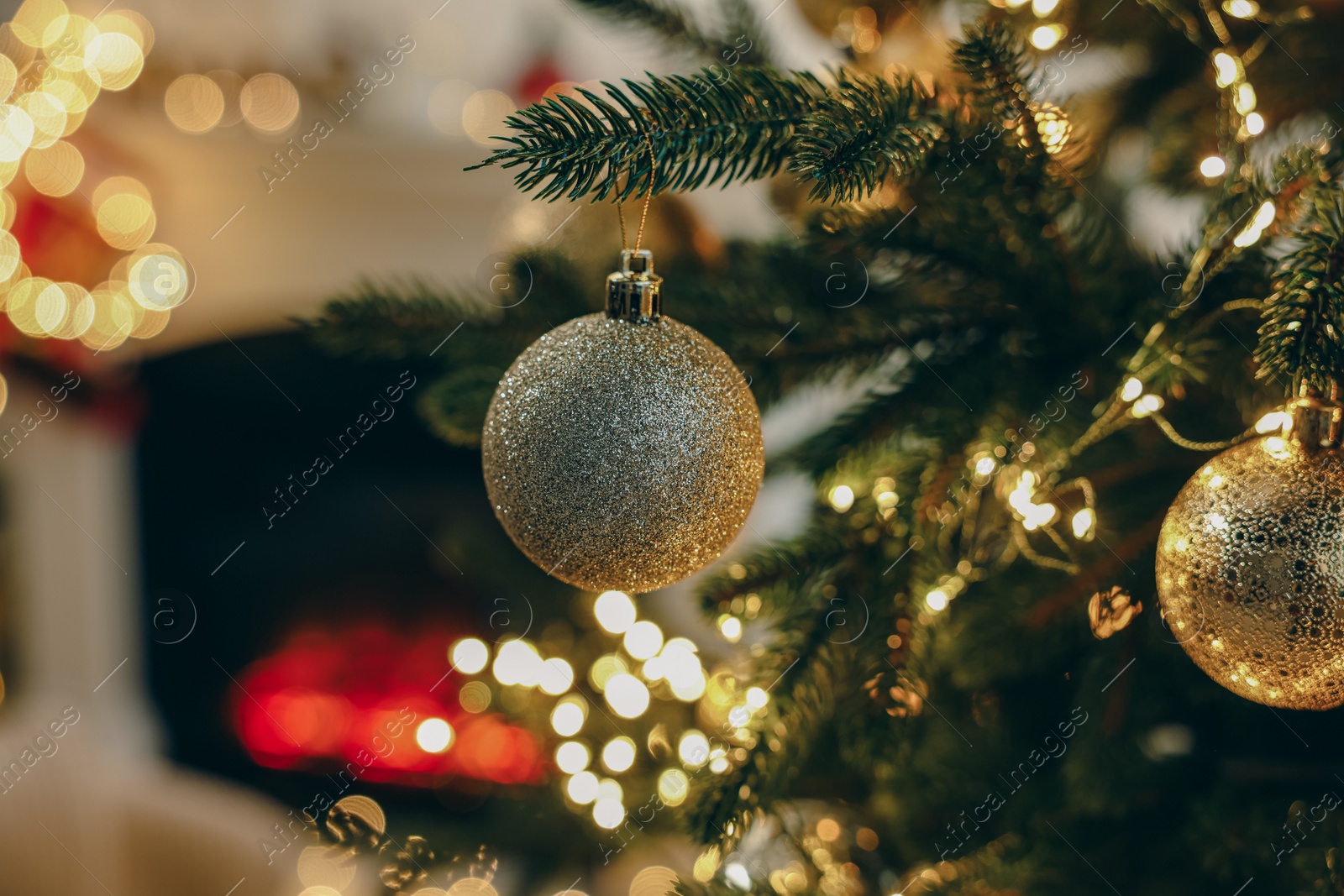 Photo of Beautiful Christmas baubles hanging on fir tree branch in room, closeup. Space for text