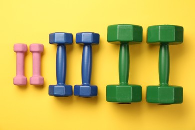 Different dumbbells on yellow background, flat lay