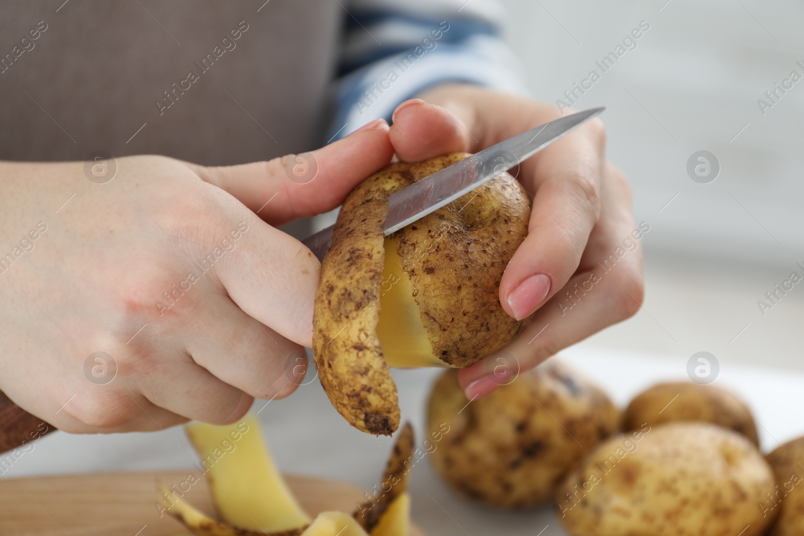 Photo of Woman peeling fresh potato with knife at table, closeup