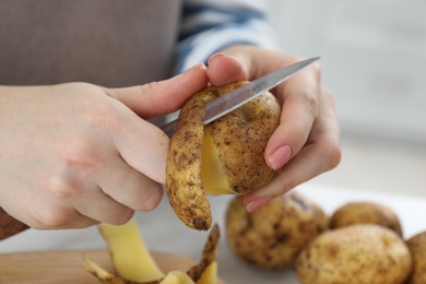 Photo of Woman peeling fresh potato with knife at table, closeup