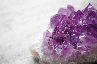 Beautiful purple amethyst gemstone on grey table, closeup view. Space for text