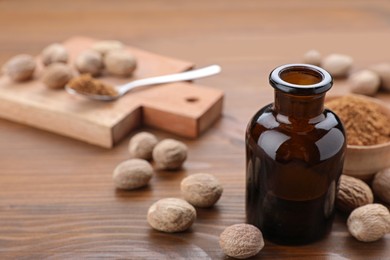 Photo of Bottle of nutmeg oil and nuts on wooden table, closeup. Space for text