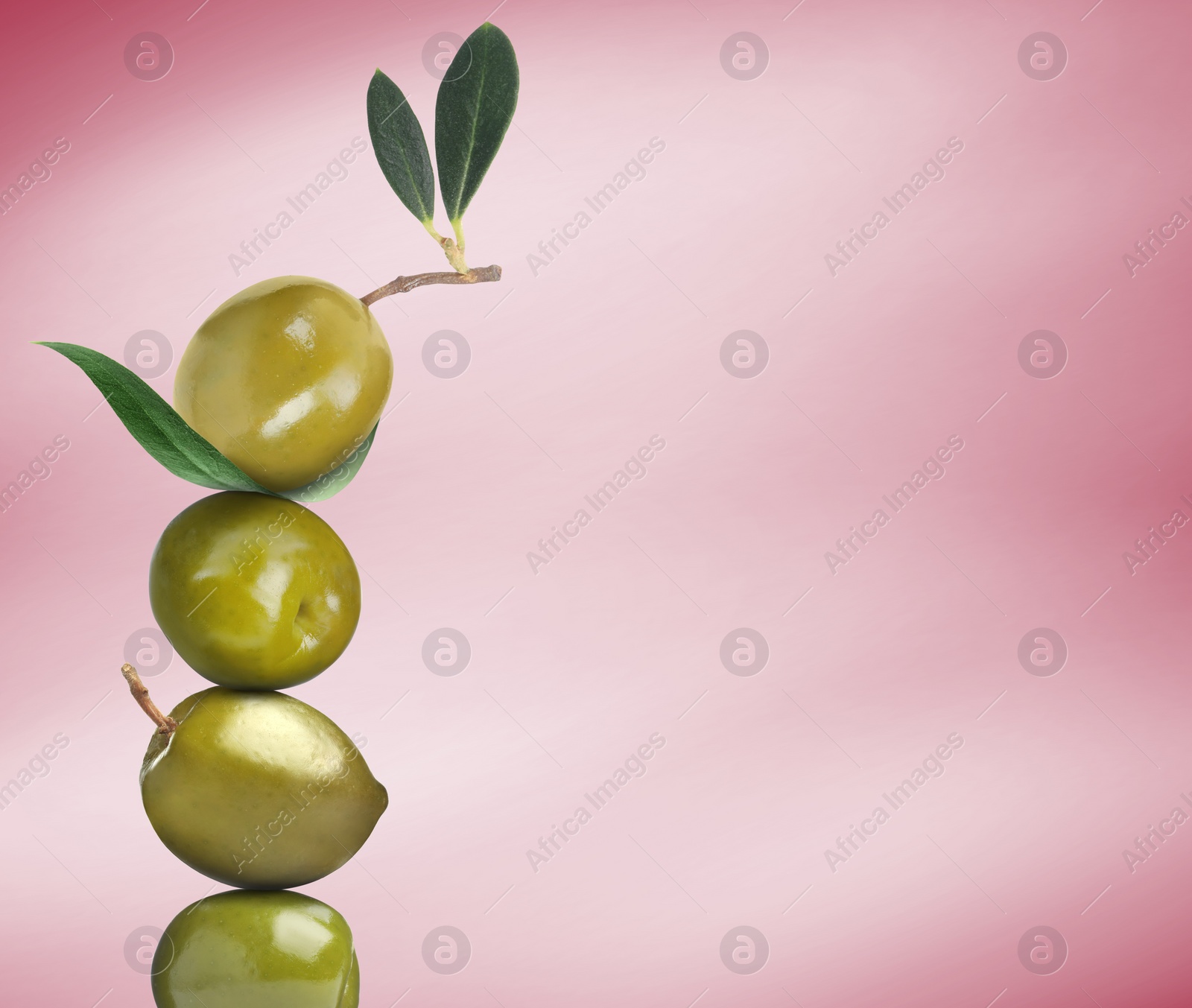 Image of Stack of whole green olives with leaves on pink gradient background, space for text