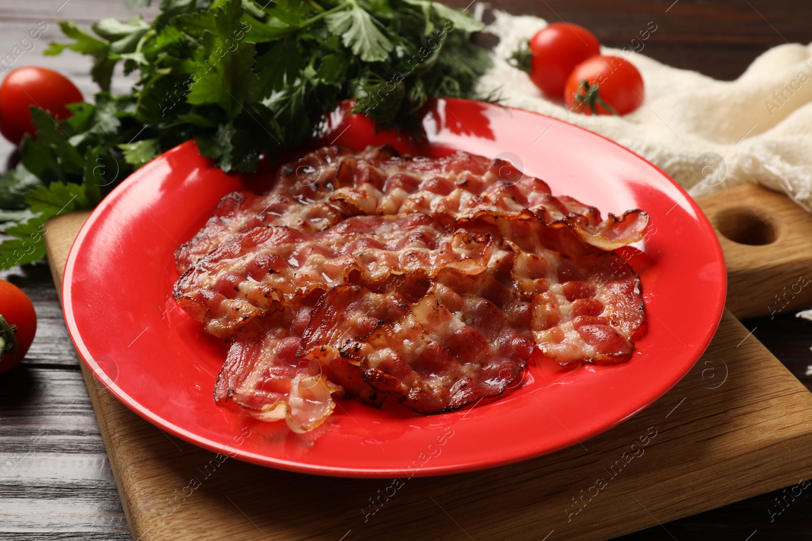 Photo of Plate with fried bacon slices, tomatoes and parsley on wooden table, closeup