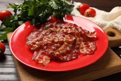 Plate with fried bacon slices, tomatoes and parsley on wooden table, closeup