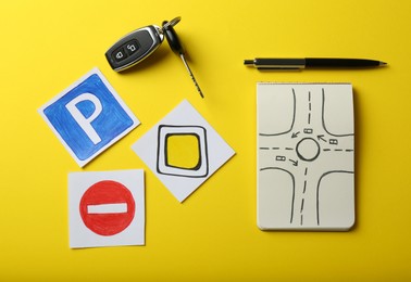 Flat lay composition with workbook for driving lessons and road signs on yellow background. Passing license exam