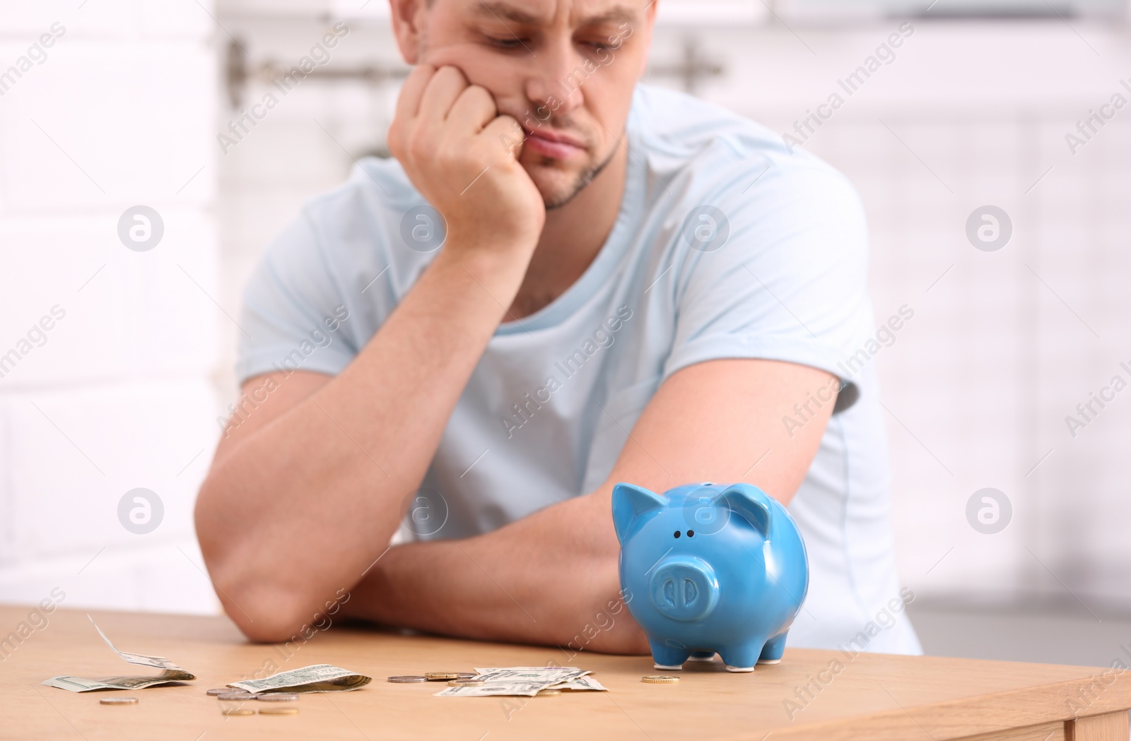 Photo of Sad man with piggy bank and money at home