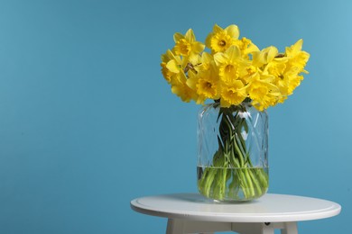 Photo of Beautiful daffodils in vase on white table against light blue background, space for text