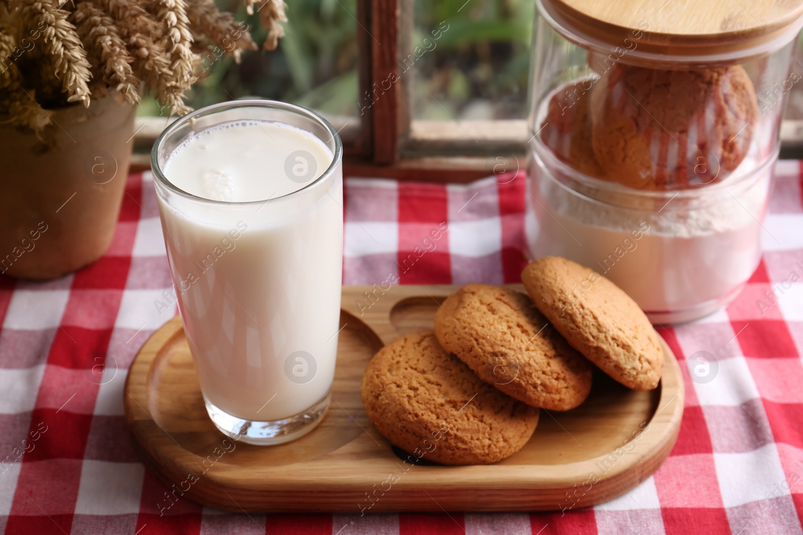 Photo of Glass of milk with cookies on red checkered tablecloth indoors