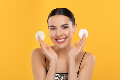 Photo of Beautiful woman holding cotton pads on orange background. Removing makeup