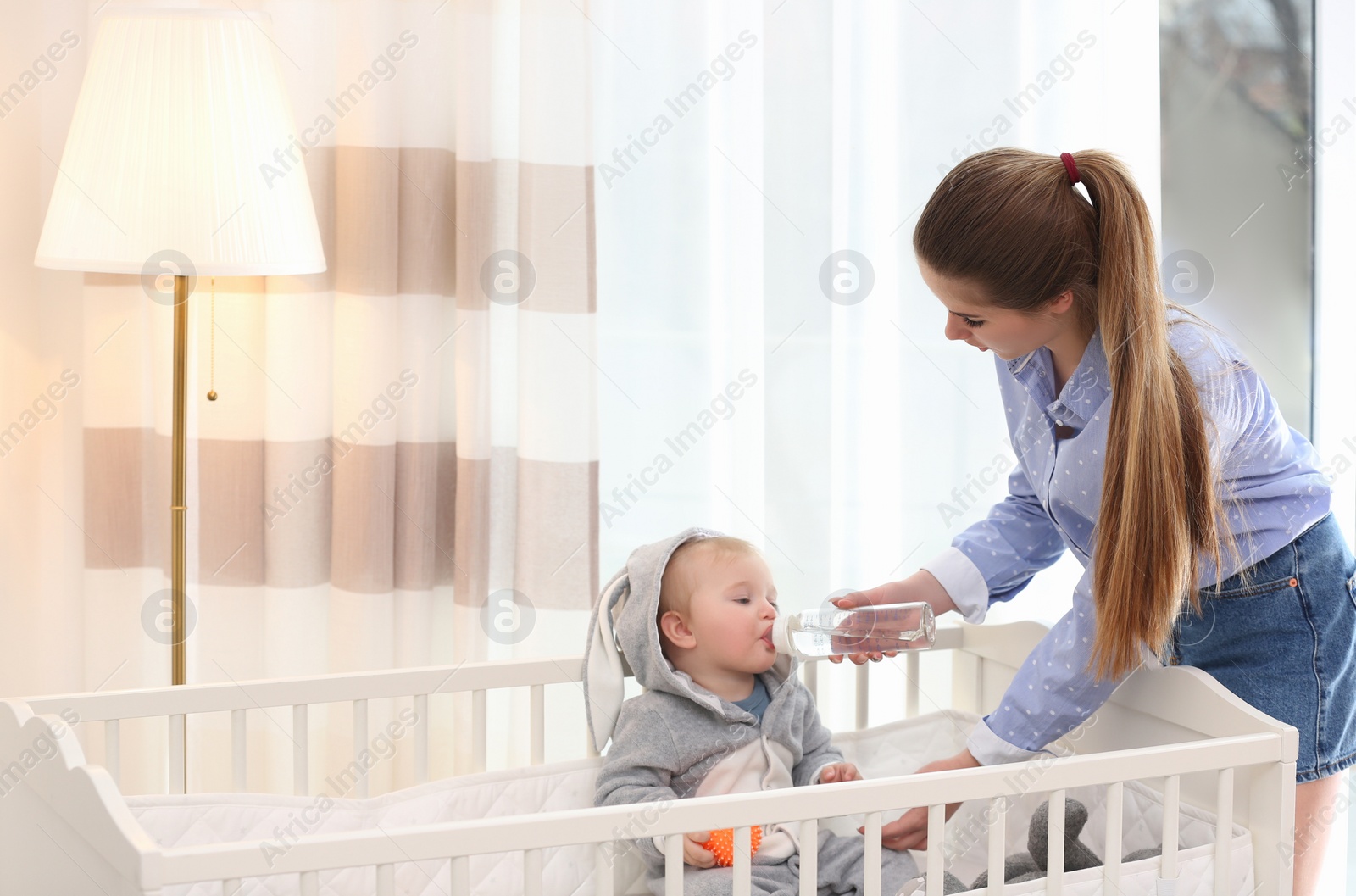 Photo of Teen nanny giving cute little baby water from bottle at home