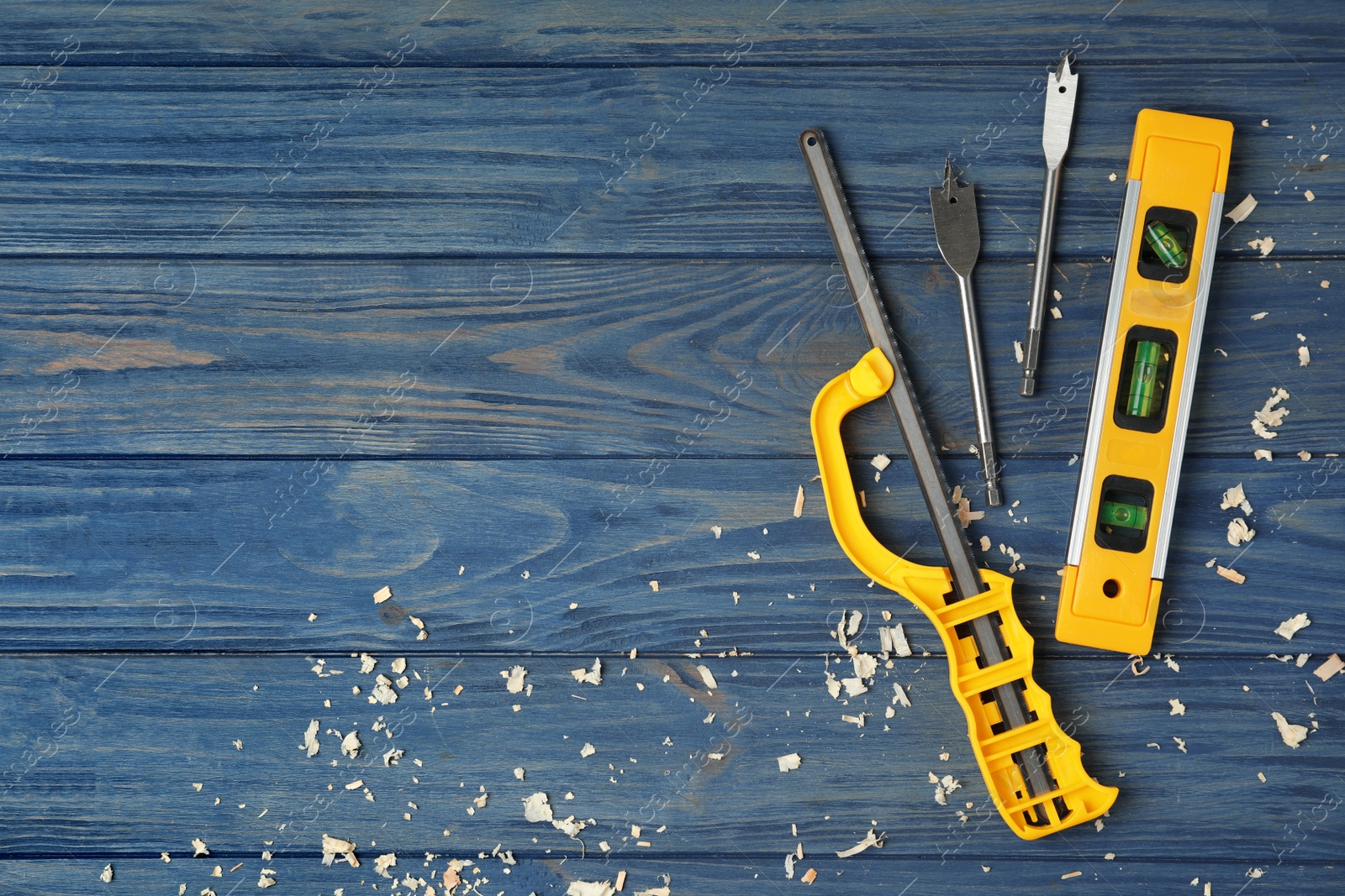 Photo of Modern carpenter's tools and shavings on blue wooden background, flat lay. Space for text