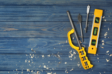 Photo of Modern carpenter's tools and shavings on blue wooden background, flat lay. Space for text