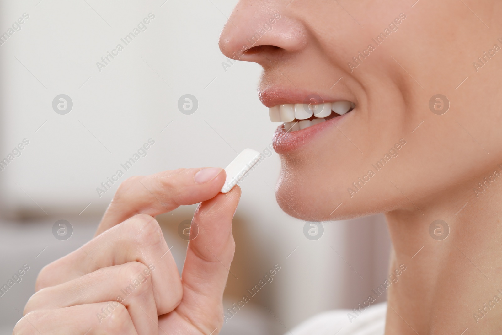 Photo of Woman putting chewing gum into mouth on blurred background, closeup