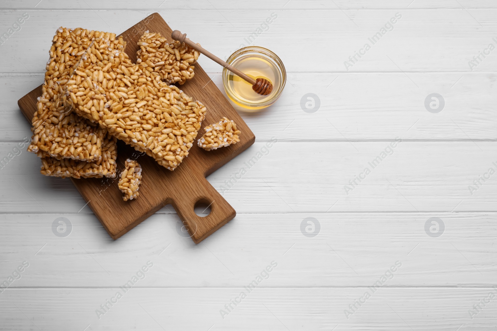 Photo of Puffed rice bars (kozinaki) and honey on white wooden table, flat lay. Space for text