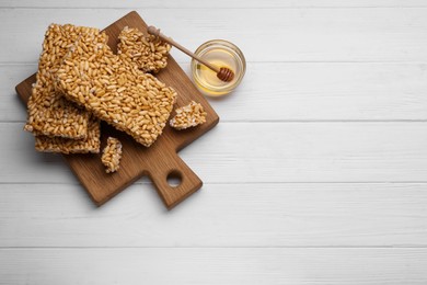 Puffed rice bars (kozinaki) and honey on white wooden table, flat lay. Space for text