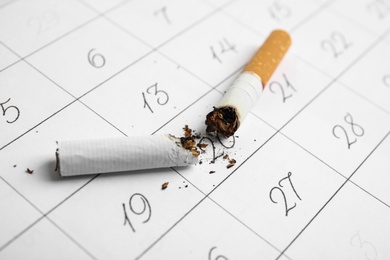 Photo of Cigarette stubs on calendar sheet. Quitting smoking concept