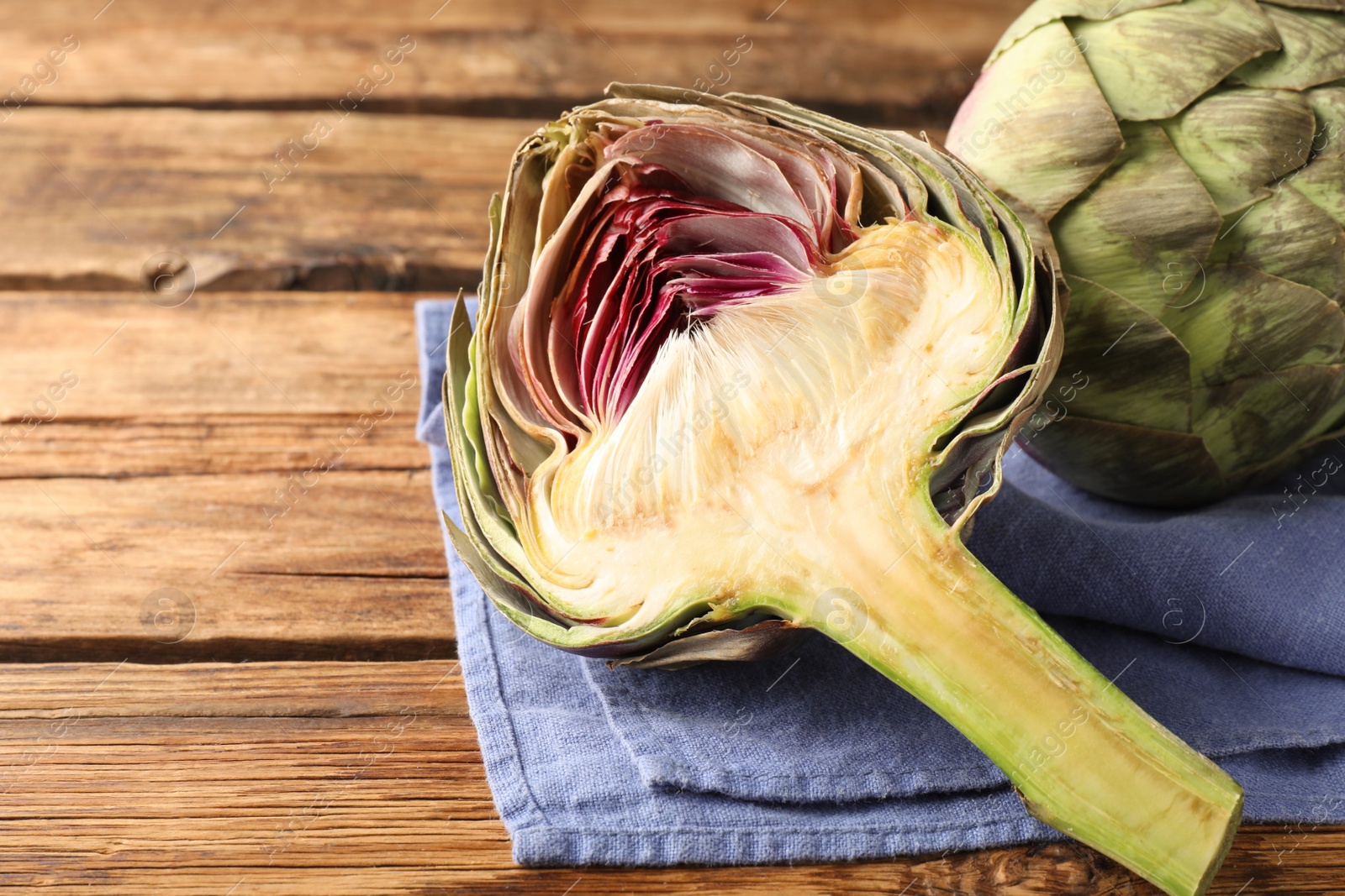 Photo of Cut and whole fresh raw artichokes on wooden table, closeup. Space for text