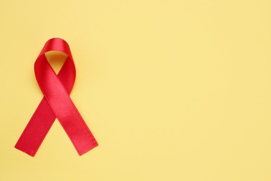 Top view of red ribbon on yellow background, space for text. AIDS disease awareness
