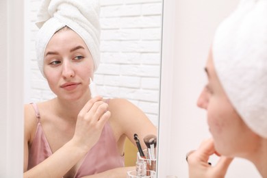 Woman with acne problem applying cream near mirror indoors