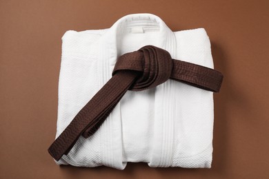 Photo of Karate belt and white kimono on brown background, top view