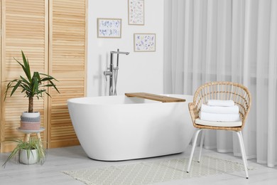 Photo of Stylish white tub and chair with towels in bathroom. Interior design
