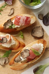 Photo of Delicious bruschettas with cheese, prosciutto and slices of black truffle on white wooden table, flat lay