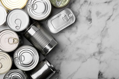 Many closed tin cans on white marble table, flat lay. Space for text