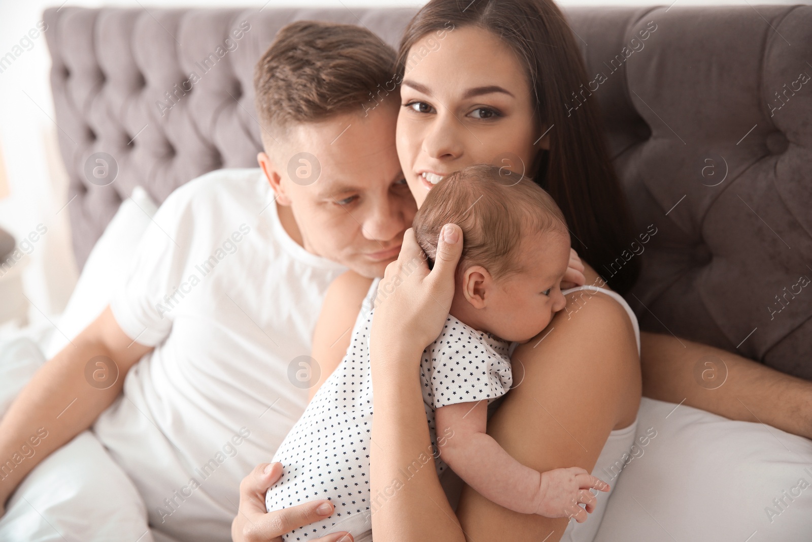 Photo of Happy couple with their newborn baby on bed