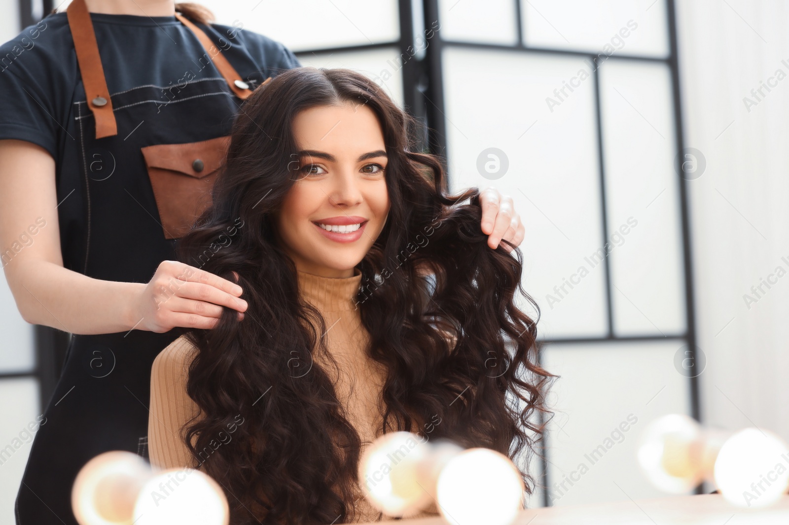 Photo of Hair styling. Professional hairdresser working with smiling client in salon, closeup. Space for text