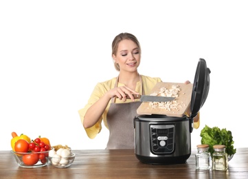 Young woman preparing food with modern multi cooker at table against white background