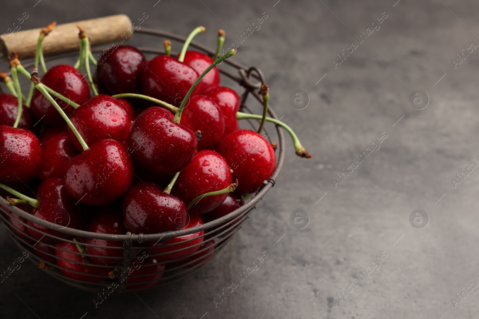 Photo of Metal basket with ripe sweet cherries on dark grey table, closeup. Space for text