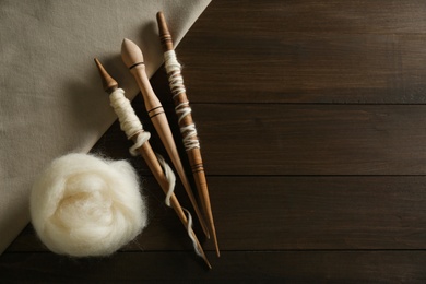 Photo of Soft white wool with spindles on wooden table, flat lay. Space for text