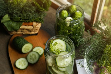 Photo of Glass jars, fresh cucumbers and herbs on wooden table indoors. Pickling recipe