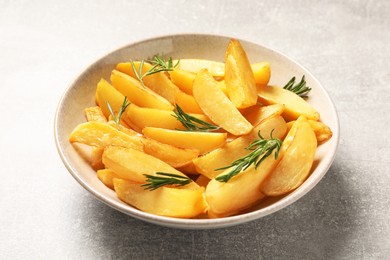 Photo of Plate with tasty baked potato wedges and rosemary on grey table, closeup