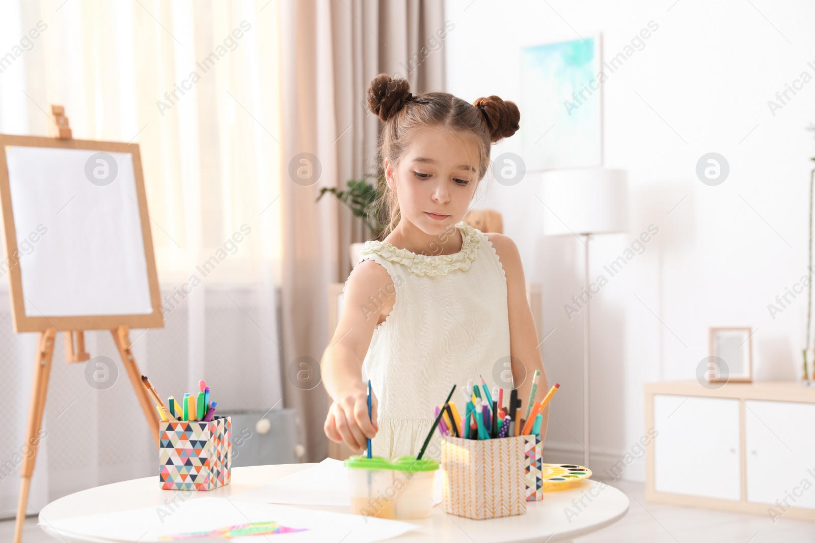 Photo of Little girl painting picture at table indoors