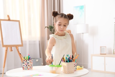 Little girl painting picture at table indoors