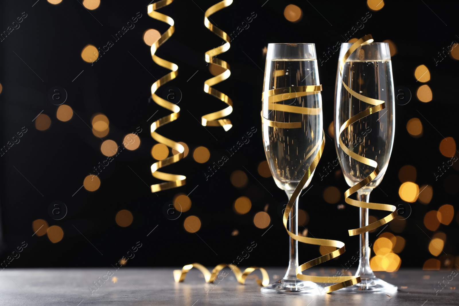 Photo of Glasses of champagne and serpentine streamers against black background with blurred lights. Space for text