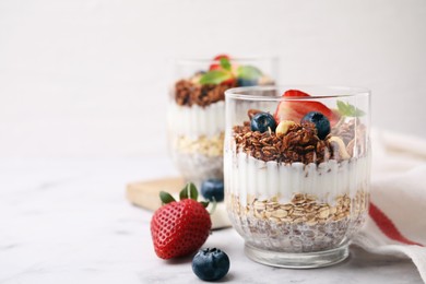 Photo of Tasty granola with berries, yogurt and chia seeds in glass on white table, space for text