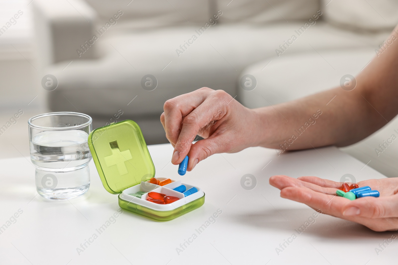 Photo of Woman with pills, organizer and glass of water at white table, closeup